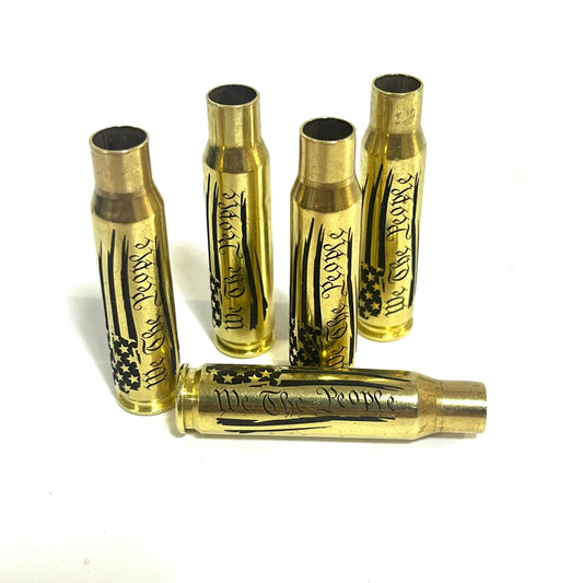 Four upright and one horizontal .308 WIN cartridge cases engraved with a We The People flag design on a white surface.