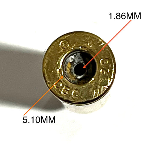 Close-up of a deprimed 308 Winchester brass casing base with orange arrows labeling the primer hole at 1.86 millimeters and flash hole area at 5.10 millimeters