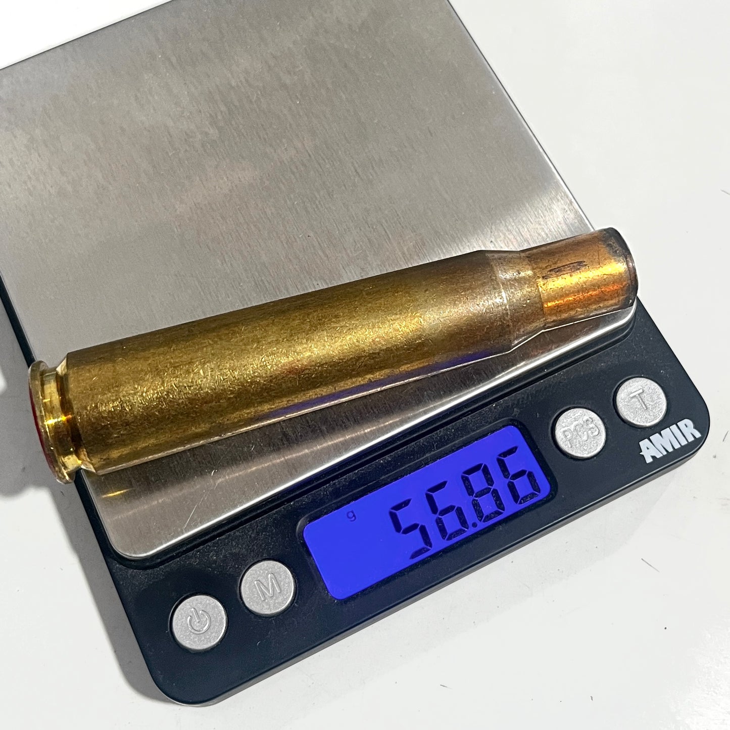 Single uncleaned 50 BMG rifle casing resting on a digital scale displaying a weight reading of 56.86 grams.