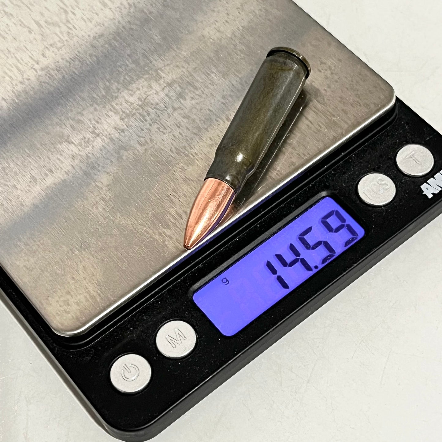 A gray steel 7.62x39 dummy shell with a copper bullet resting on a digital scale reading 14.59 grams.