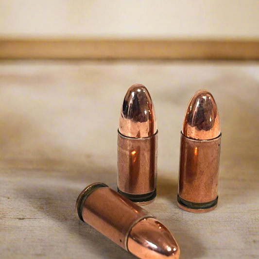 3 copper 9mm Luger dummy rounds, two standing and one lying, on a wood table