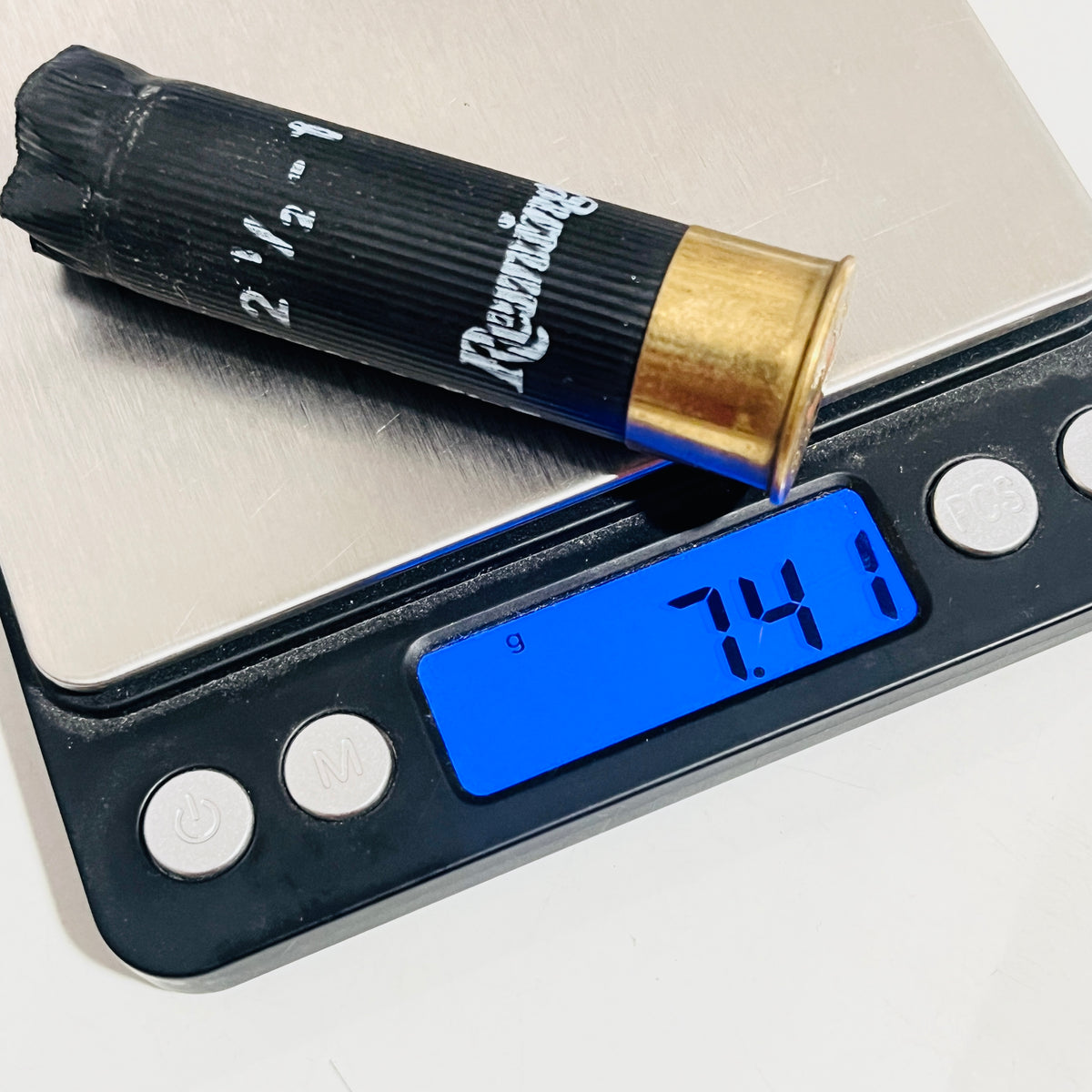 Spent black Remington shotgun shell with brass base resting on a digital scale reading 7.41 grams