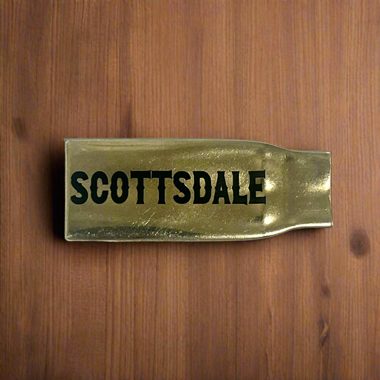 Flattened brass .308 casing engraved with Scottsdale in black lettering on a wood surface