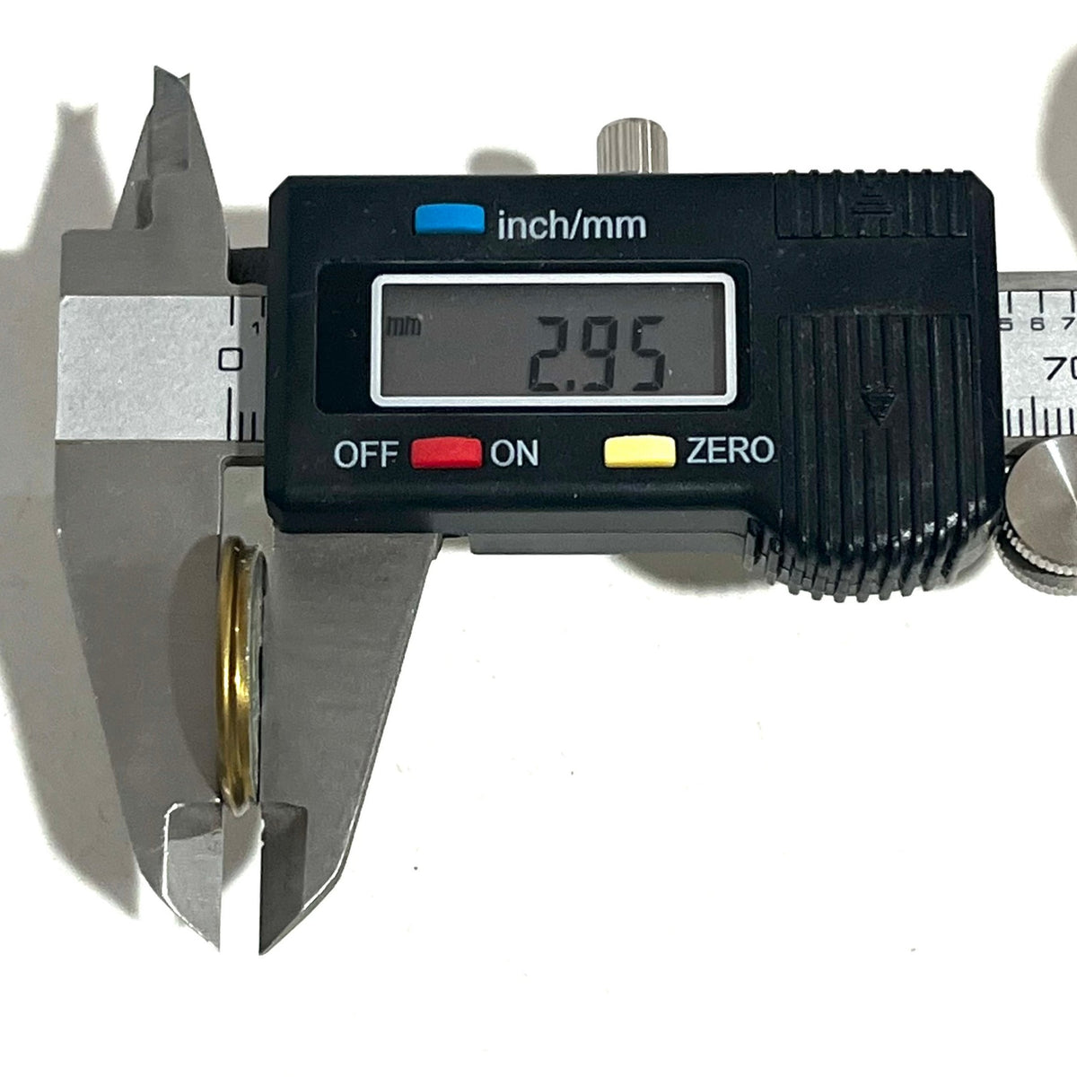Digital caliper measuring the thickness of a brass shotgun shell slice showing 2.95 mm