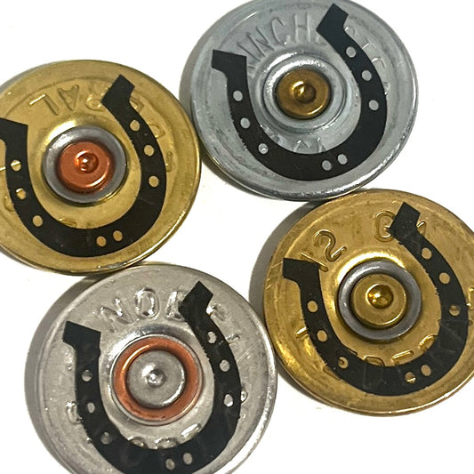 Close-up of four gold and silver 12 gauge shotgun shell slices with black engraved horseshoe designs on a white background
