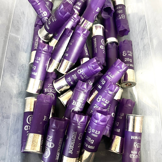 A large pile of purple Bornaghi shotgun shells with silver high brass bottoms in a plastic bin
