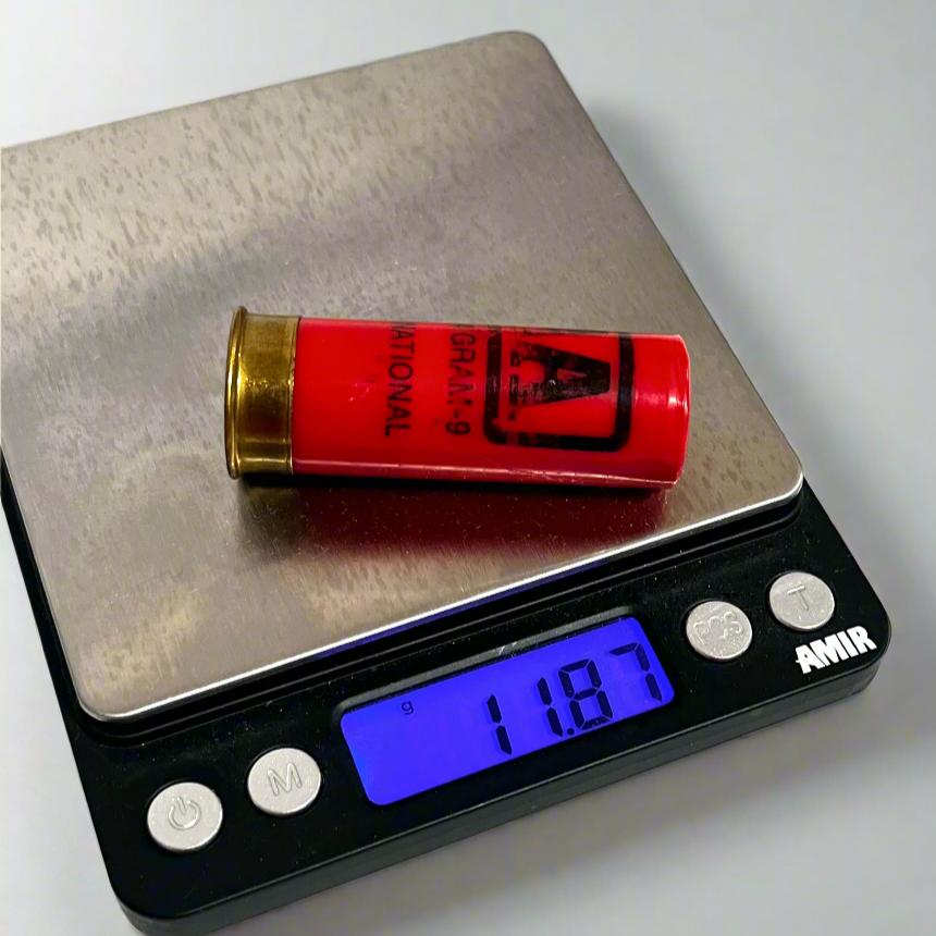Single red Winchester AA International 12 gauge shotgun dummy round on a digital gram scale reading 11.87 grams