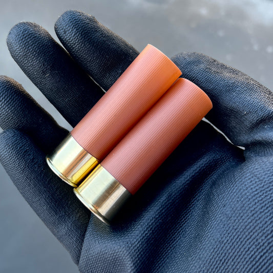 Empty Shotgun Shells rose gold 12 gauge blank hulls held in a gloved hand, showing smooth unmarked plastic and high brass.