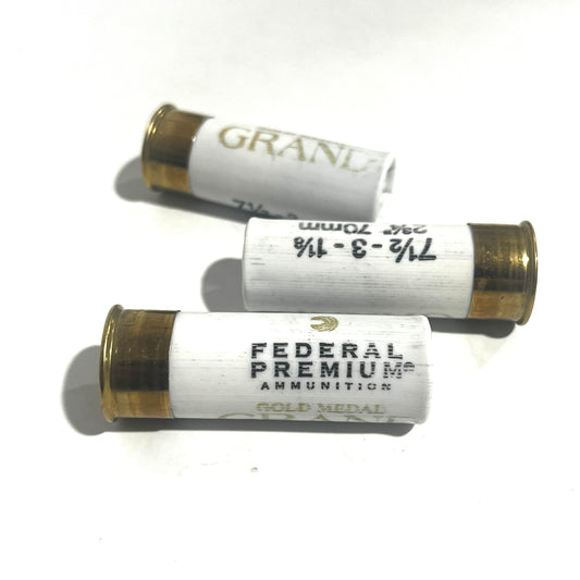 Three white Federal Premium Gold Medal Grand 12 gauge dummy shotgun shells with gold bases on a white background