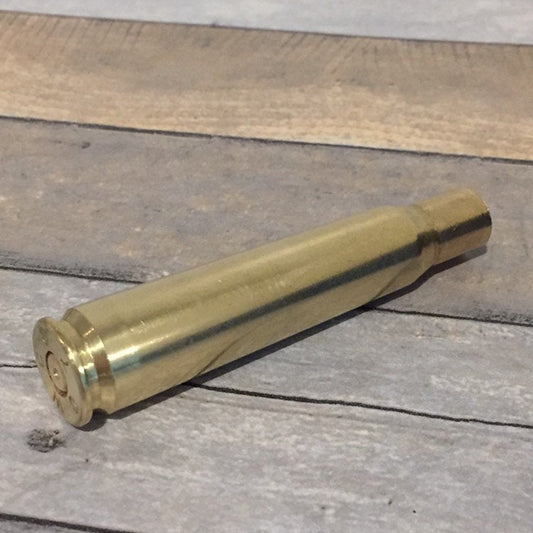 Polished .50 BMG brass shell lying on gray wood planks, base and rim angled toward the camera