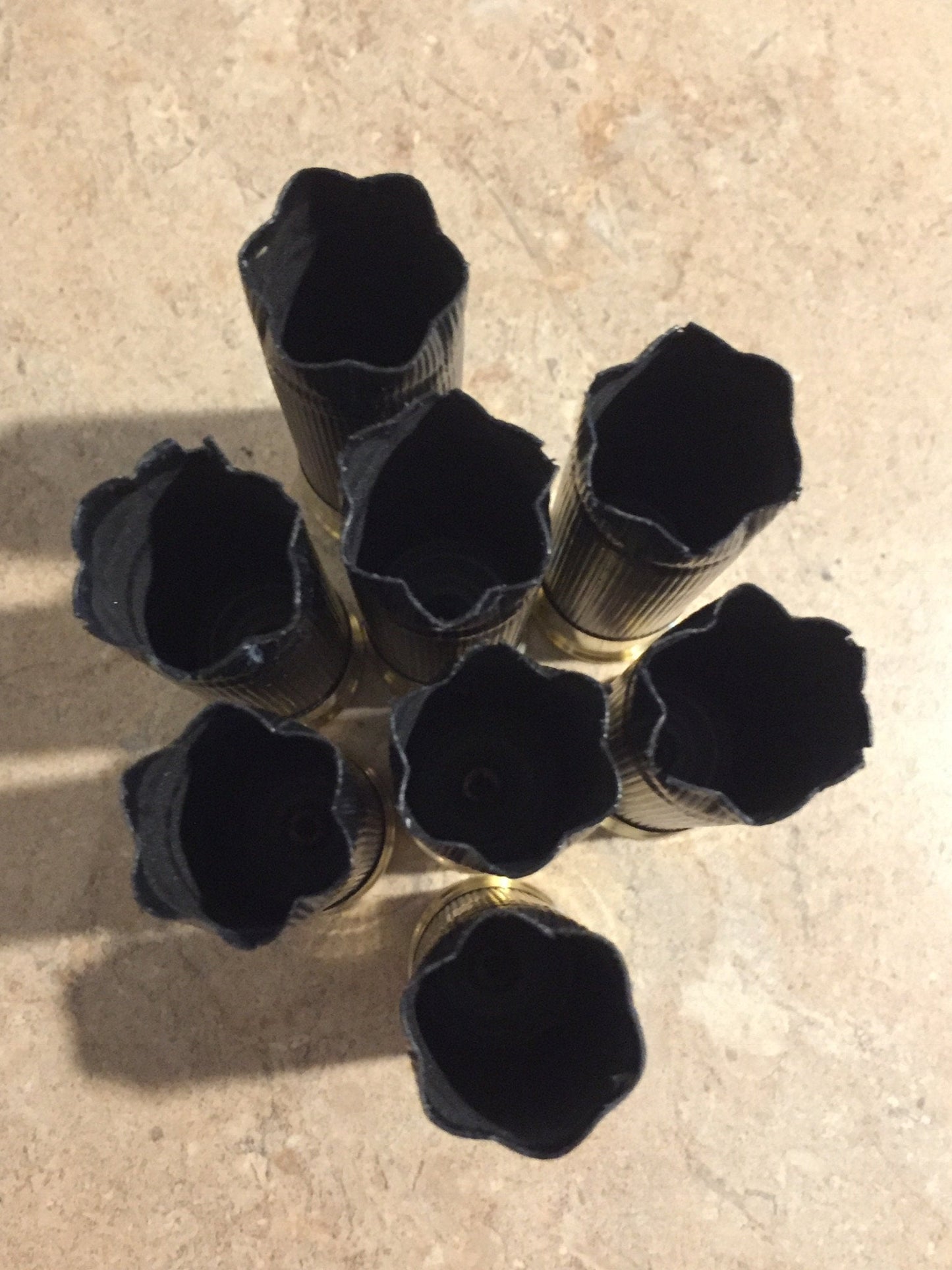 Seven black shotgun hulls arranged in a star pattern viewed from above 6 star crimp on a stone surface