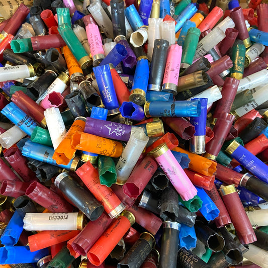 Close-up pile of mixed-color empty 12 gauge shotgun shells with brass and silver bases
