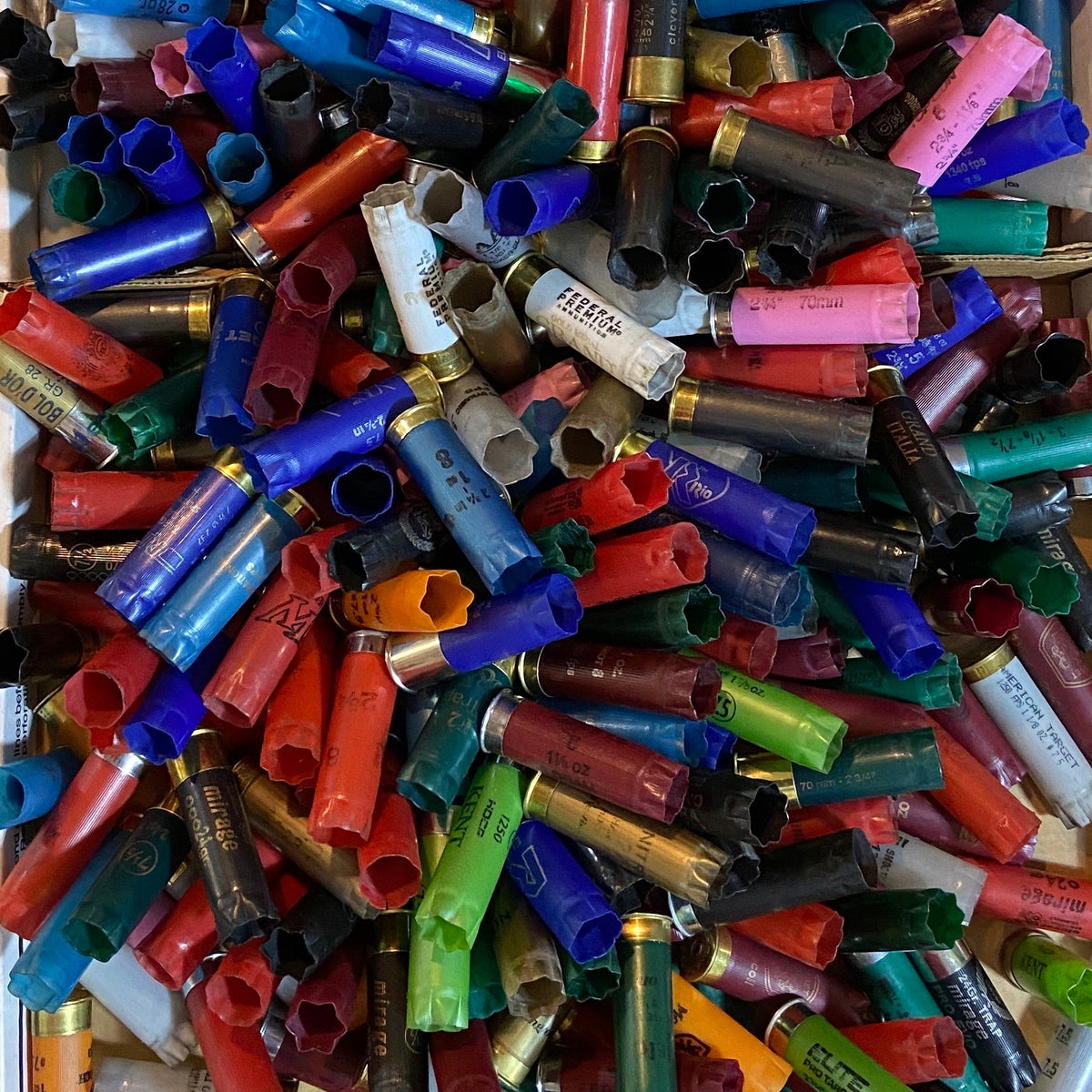 Top-down view of multi-colored 12ga shells in a tray. Inert 12ga hulls for crafts (no powder/primers).