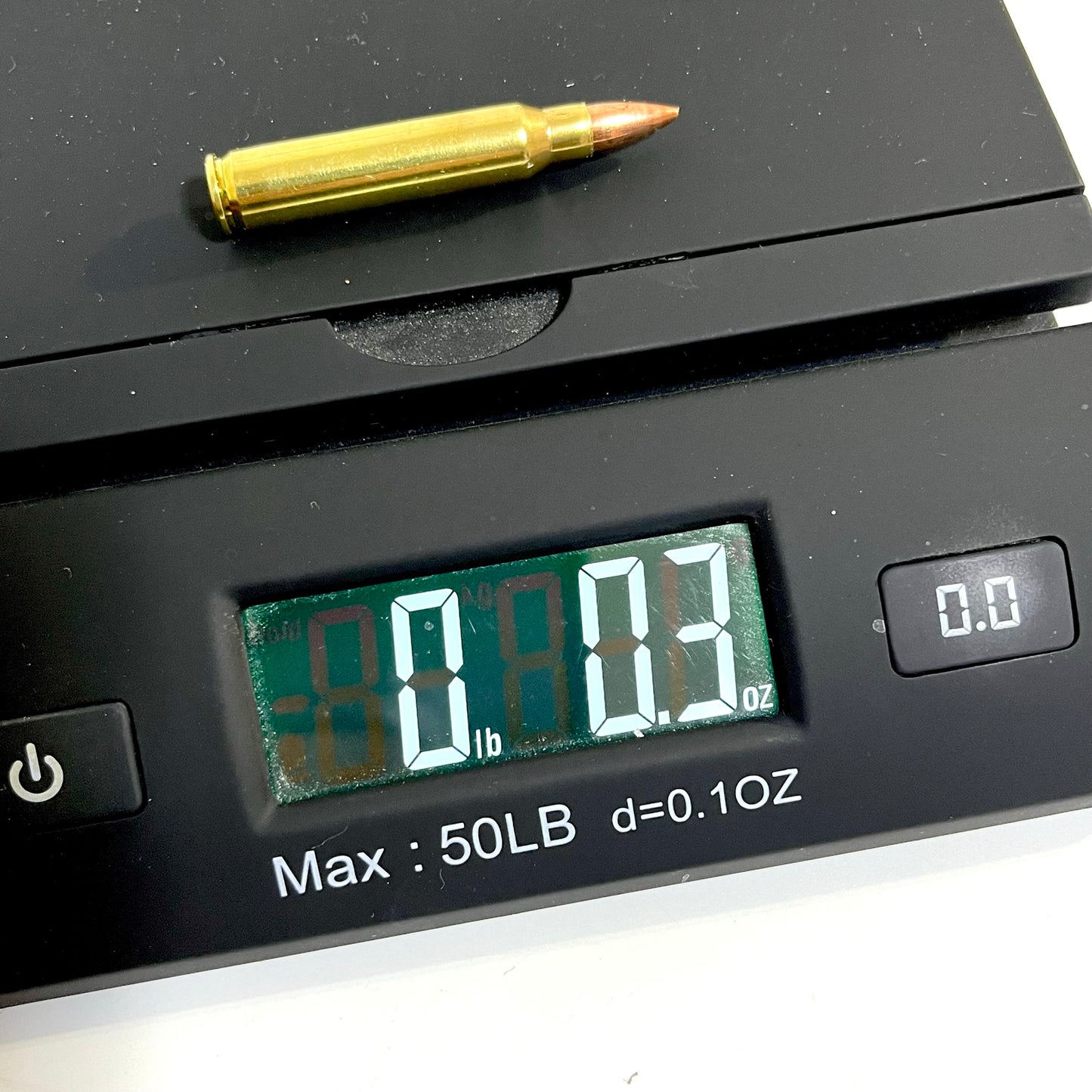 A single brass dummy cartridge placed on a digital scale, showing a weight reading of 0.3 oz.