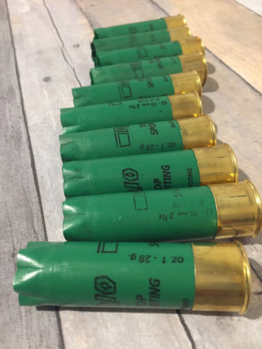 Row of empty green 12 gauge RIO Top Sporting shotgun shells with brass bases lying on a wood deck