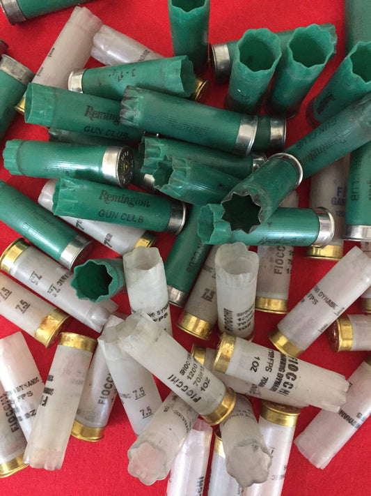 Close-up pile of green and translucent 12 gauge shotgun shell hulls on a red background