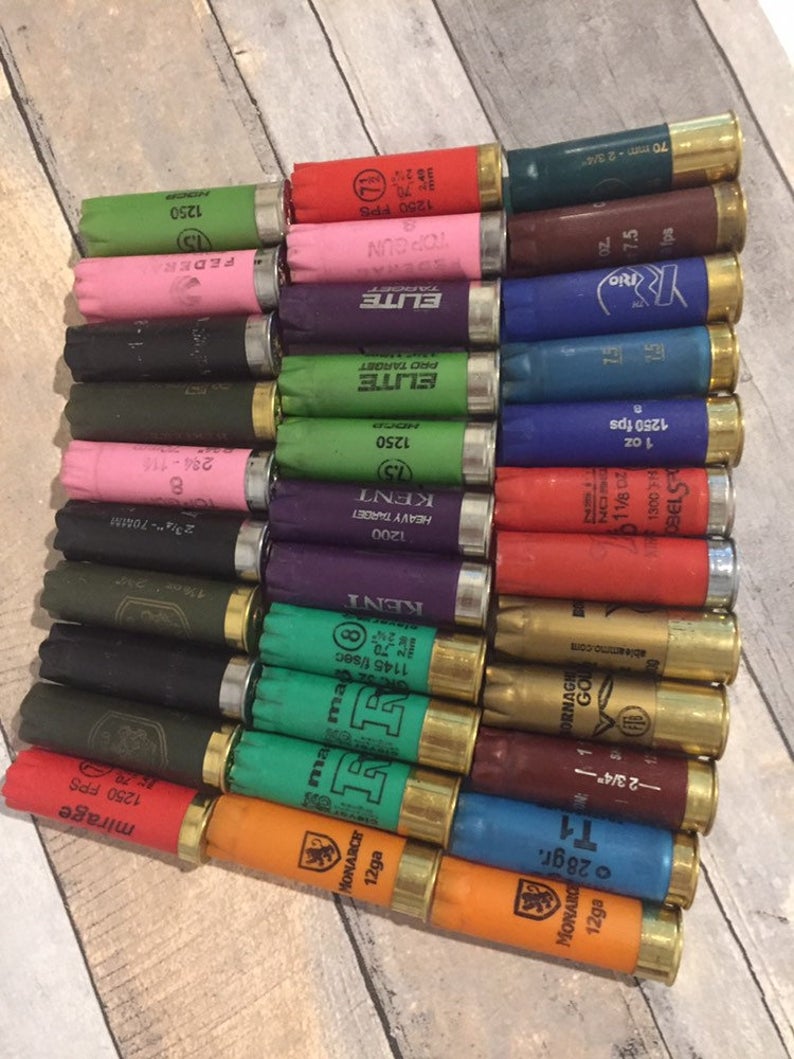 Multiple rows of mixed color empty 12 gauge shotgun hulls including red, green, blue, pink, and orange on grey wood.