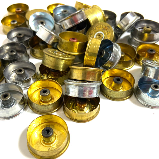 A pile of mixed gold and silver-colored 12 gauge shotgun shell cut bottoms.