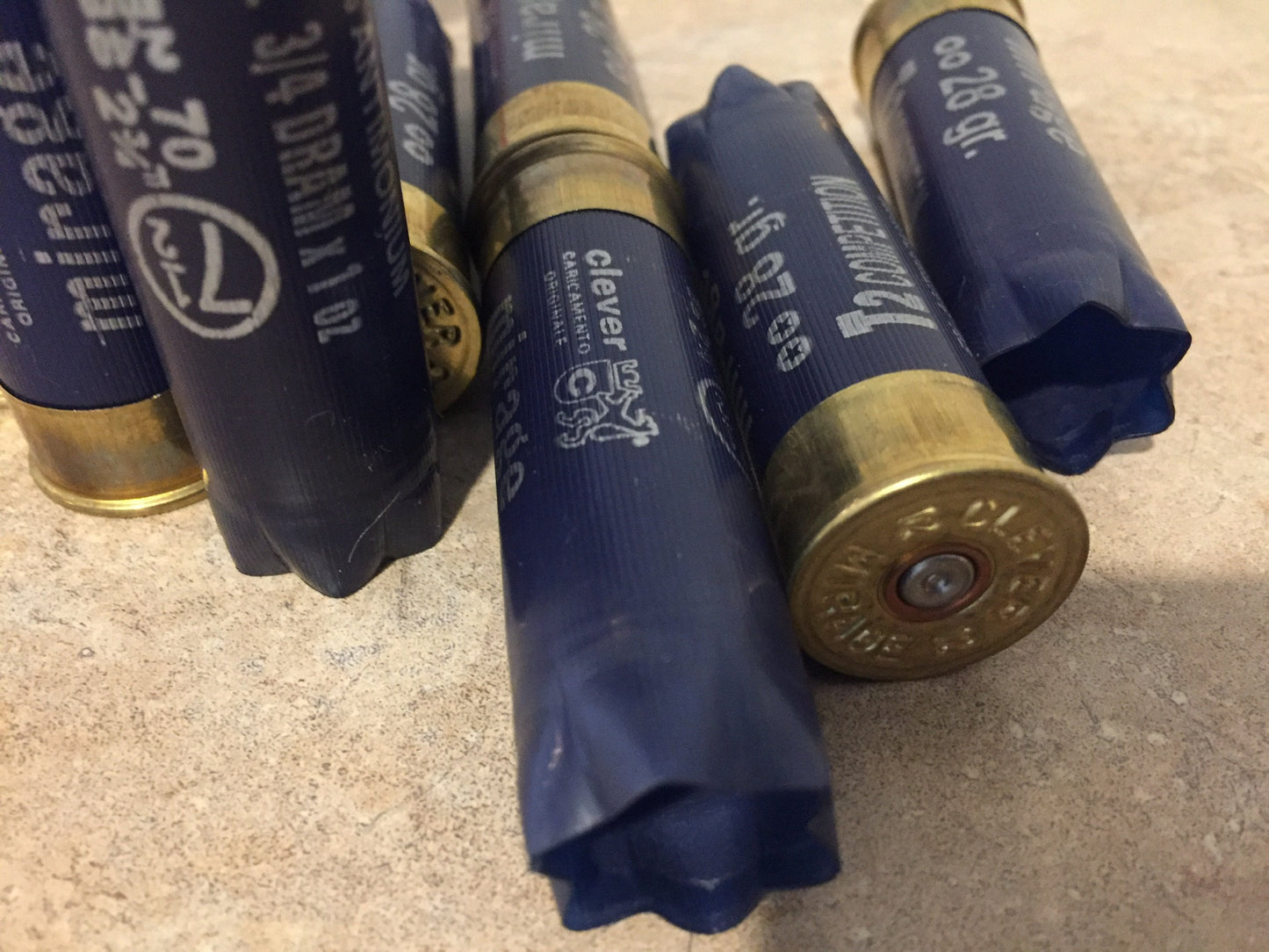 Empty navy blue 12 gauge Clever Mirage and T2 Competition shotgun shells with brass bases on a stone surface