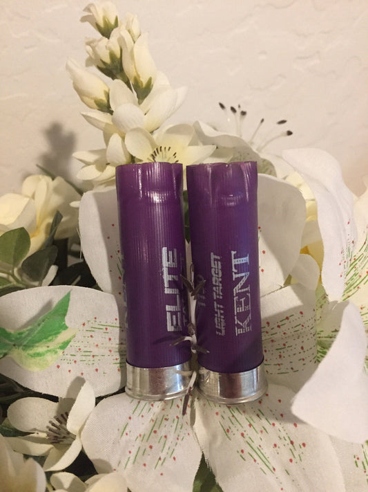 Two purple Kent Elite Target 12 gauge shotgun shells with silver heads standing among white flowers