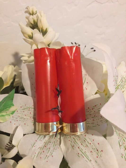 Two red plastic 12 gauge shotgun shells with gold brass heads standing among white flowers