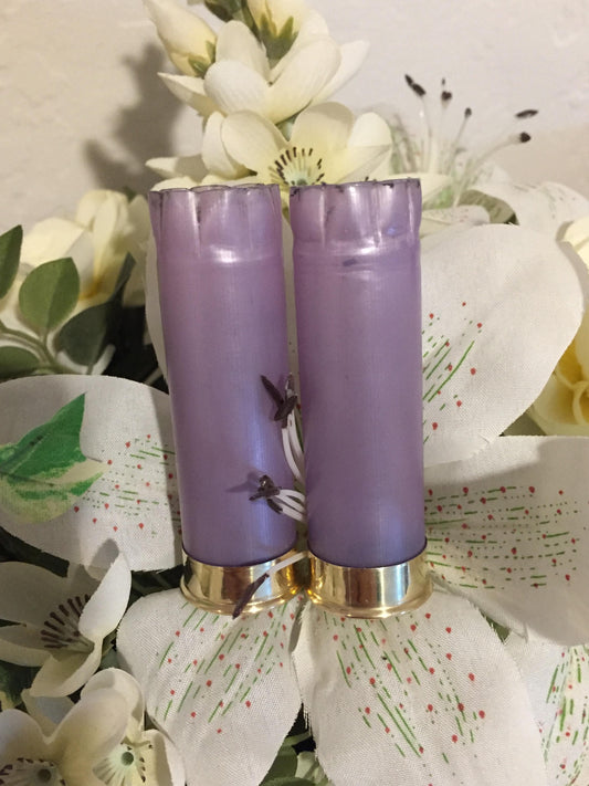 Two violet 12 gauge shotgun shells with gold brass heads standing among white flowers