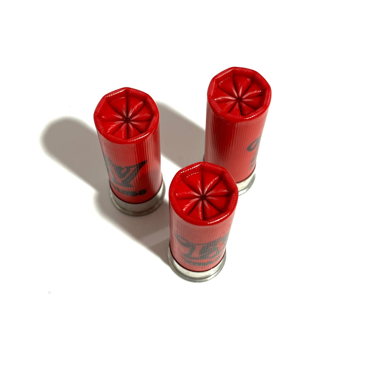 Three red 12 gauge shells standing upright showing their crimped star tops on a white surface.
