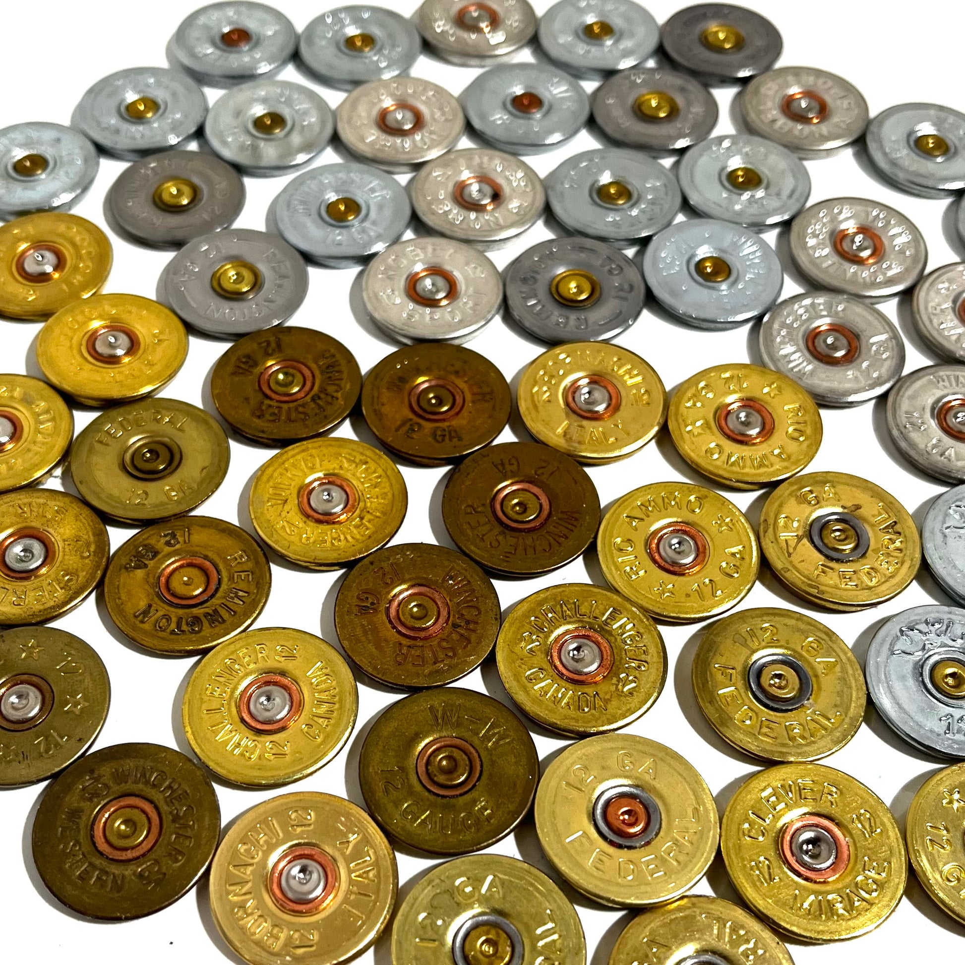 Large group of 12 gauge shotgun shell headstamp slices sorted into silver top and gold bottom sections on white.