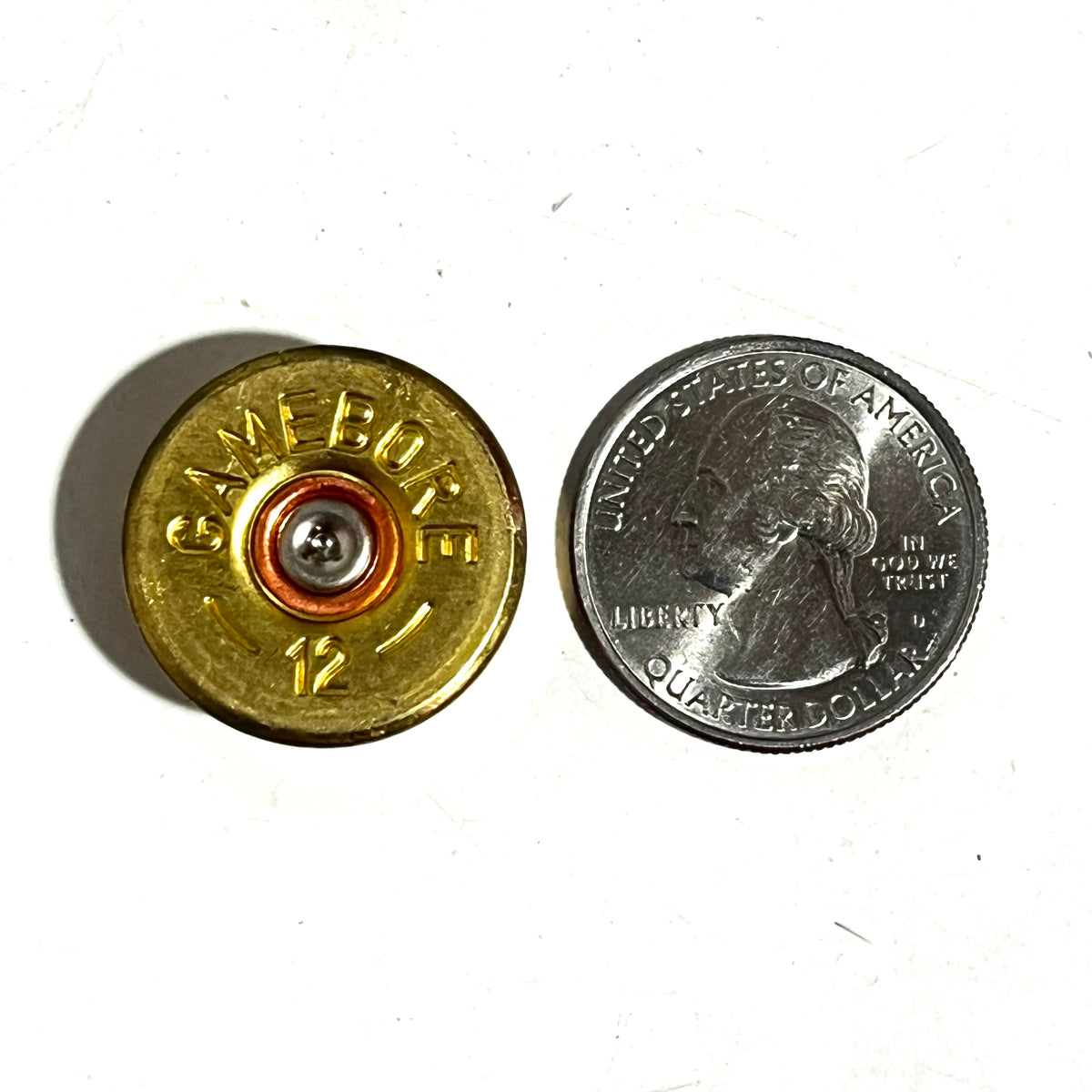 12ga brass headstamp next to a US quarter for size reference on a white surface.