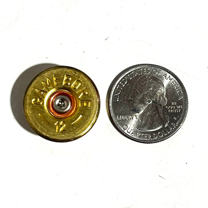 12ga brass headstamp next to a US quarter for size reference on a white surface.