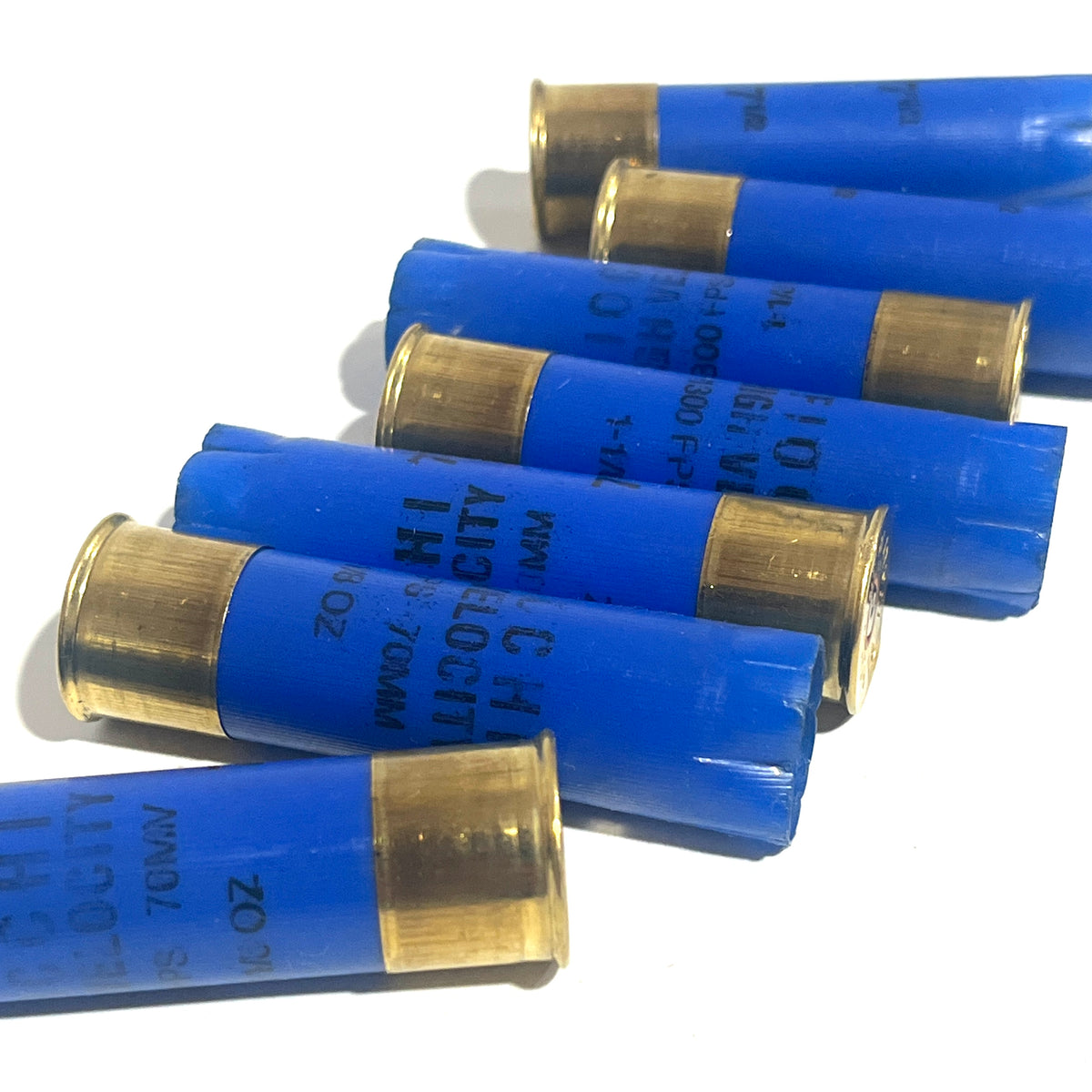 Seven blue 16 gauge empty shotgun shells with gold high brass bases lying on a white background