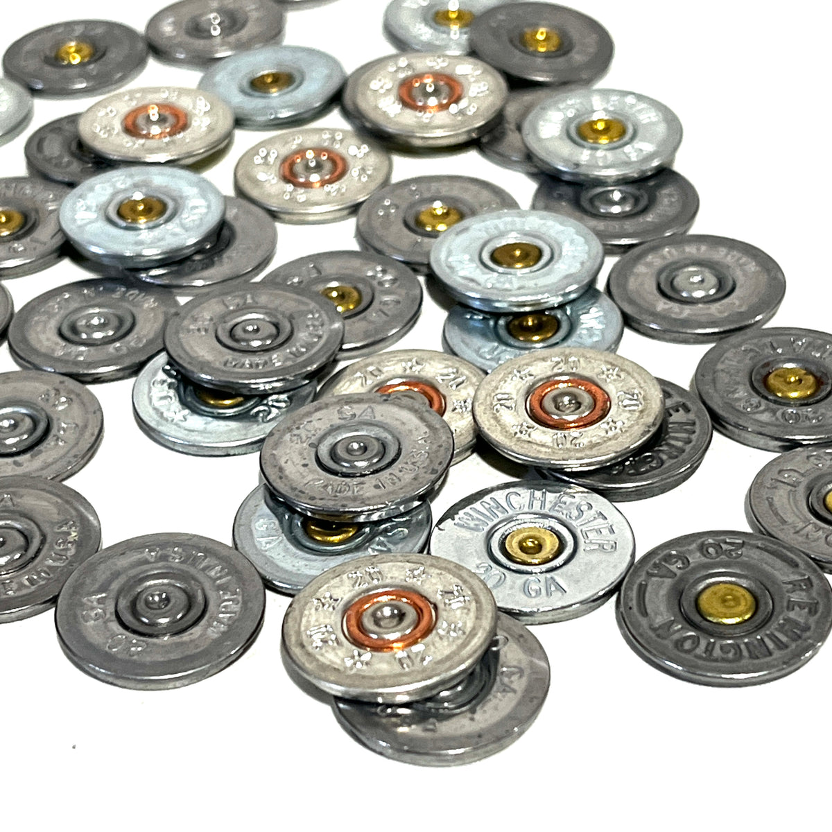 Pile of silver 20 gauge shotgun shell slices with brass primers, viewed at an angle on a white background