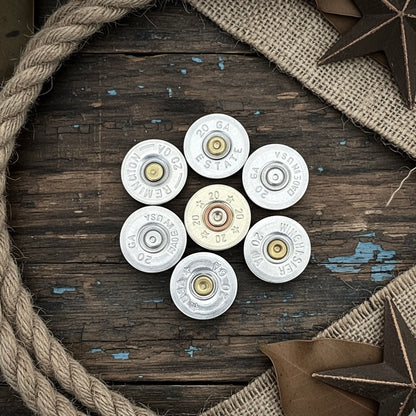 7 silver 20 gauge shotgun shell slices with various headstamps, arranged in a circle on a wood surface with rope and star decorations