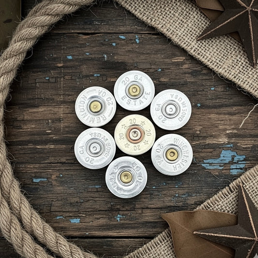 7 silver 20 gauge shotgun shell slices with various headstamps, arranged in a circle on a wood surface with rope and star decorations