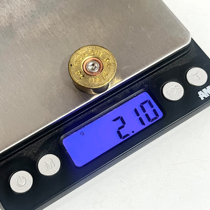 A brass headstamp case resting on a digital scale with a blue display showing 2.10 grams.
