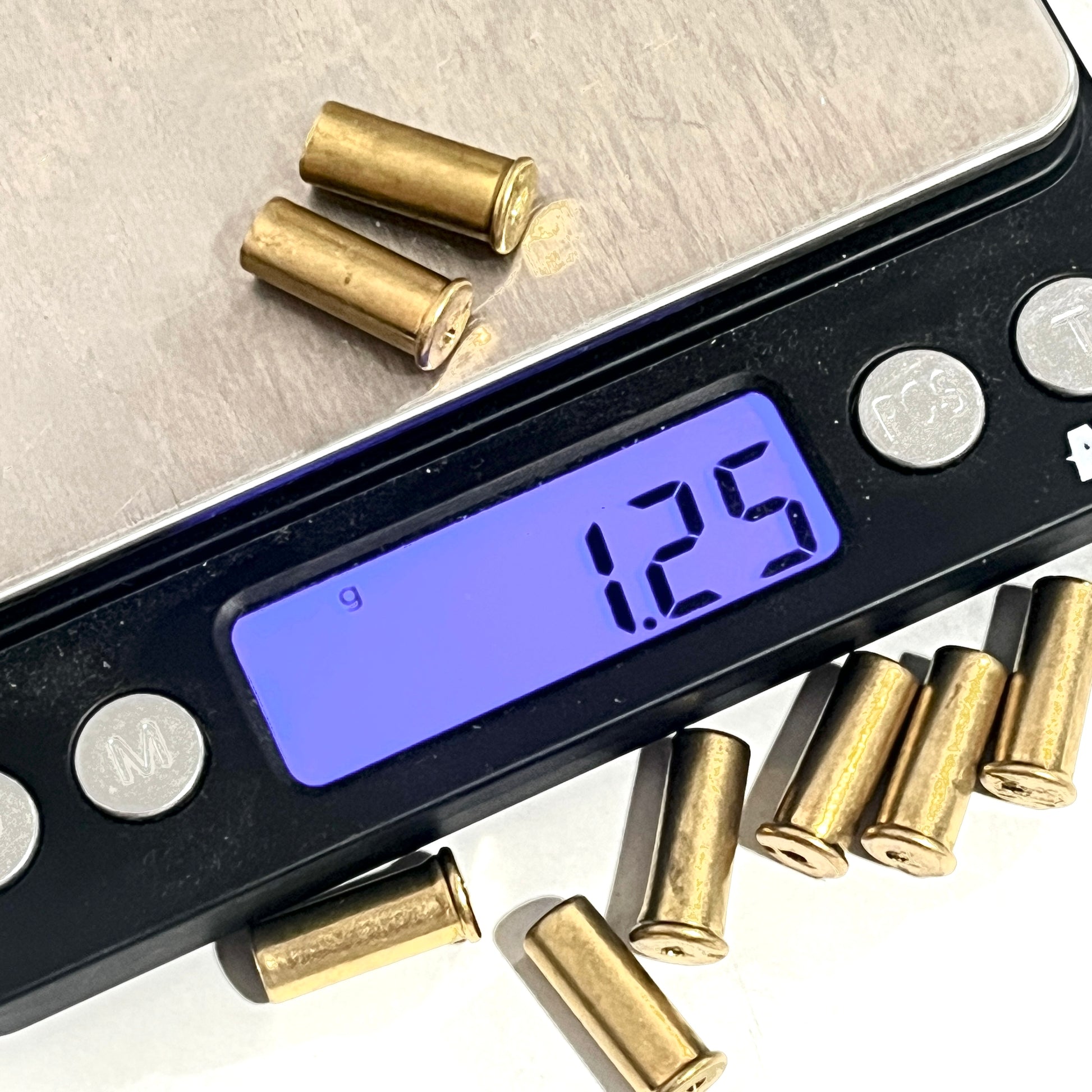A digital scale weighing a pair of gold-colored .22 caliber brass shell casings, with a reading of 1.25 grams.
