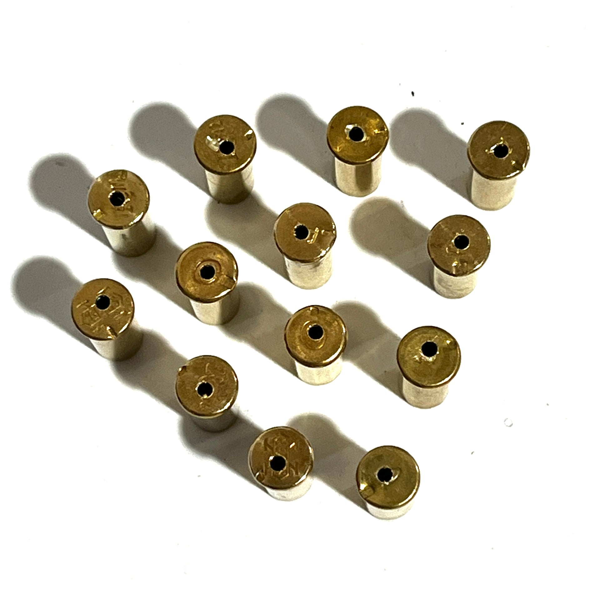 A group of authentic, once-fired .22 caliber brass shells standing upright. Each shell shows visible fired wear, spent rim strikes on the edges, and a precision-drilled hole in the side of the casing.
