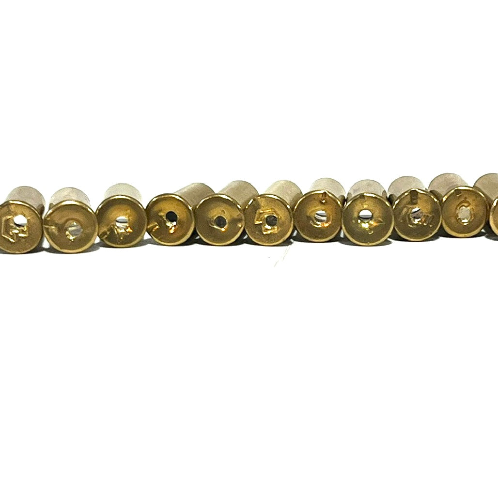 A long row of authentic, once-fired .22 caliber brass shells lying horizontally. The image focuses on the bases of the shells, showing visible fired wear and distinct spent rim strikes on the edges. Each casing features a precision-drilled hole in the side.