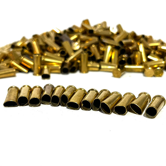 Row of open brass shell casings lined up in front of a large blurred pile of loose brass casings