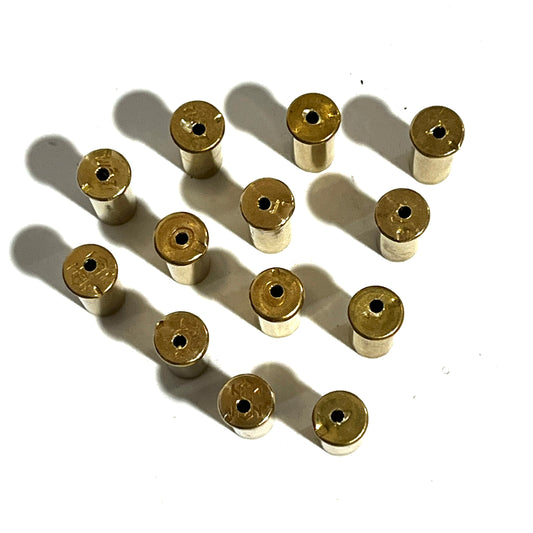 A group of authentic, once-fired .22 caliber brass shells standing upright. Each shell shows visible fired wear, spent rim strikes on the edges, and a precision-drilled hole in the side of the casing.
