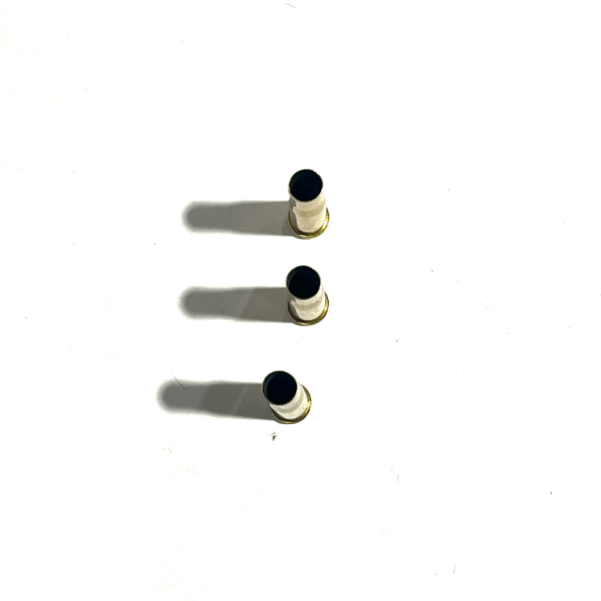 3 white-coated .22 Hornet shell casings standing upright with drilled black holes at the mouth, top-down view