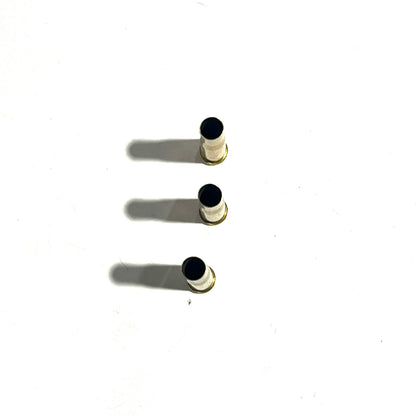 3 white-coated .22 Hornet shell casings standing upright with drilled black holes at the mouth, top-down view