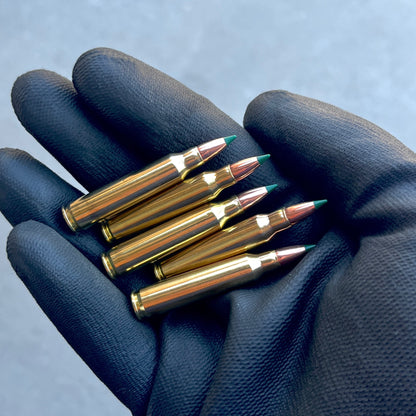Five inert 5.56 prop cartridges with green tips resting parallel on the palm of a black textured glove.