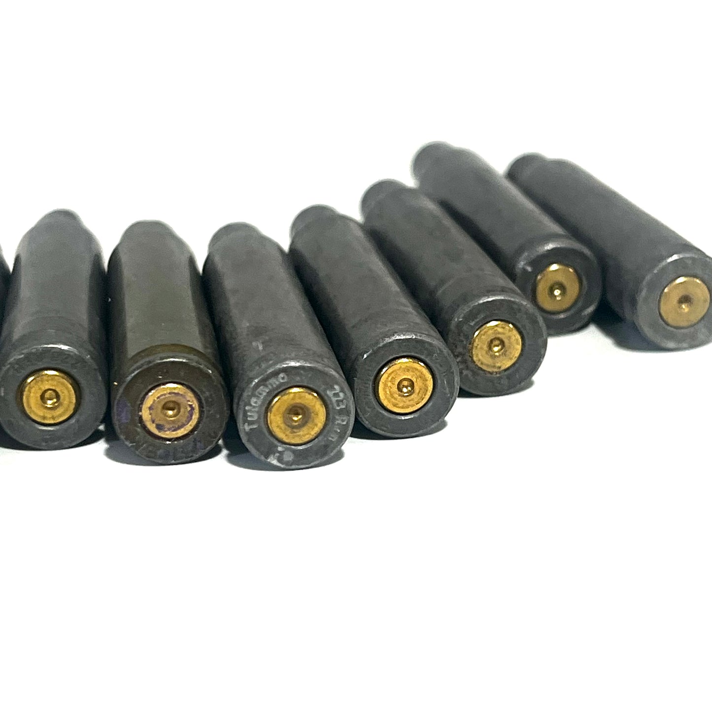 Row of gray steel .223/5.56 spent casings viewed from base showing primer pockets, on white background