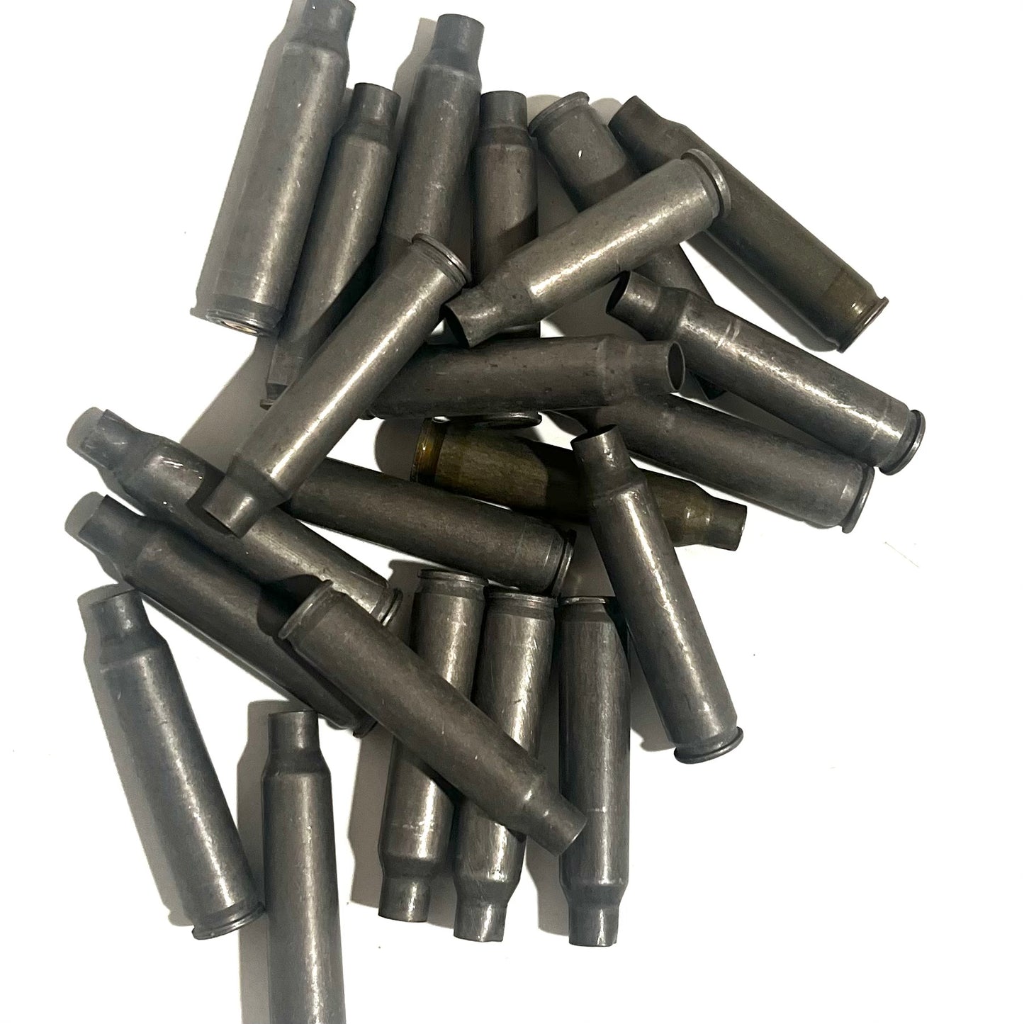 Pile of gray steel .223/5.56 spent casings scattered on white background, one brass casing mixed in