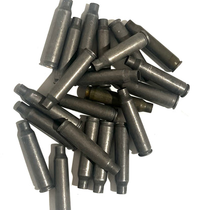 Pile of gray steel .223/5.56 spent casings scattered on white background, one brass casing mixed in
