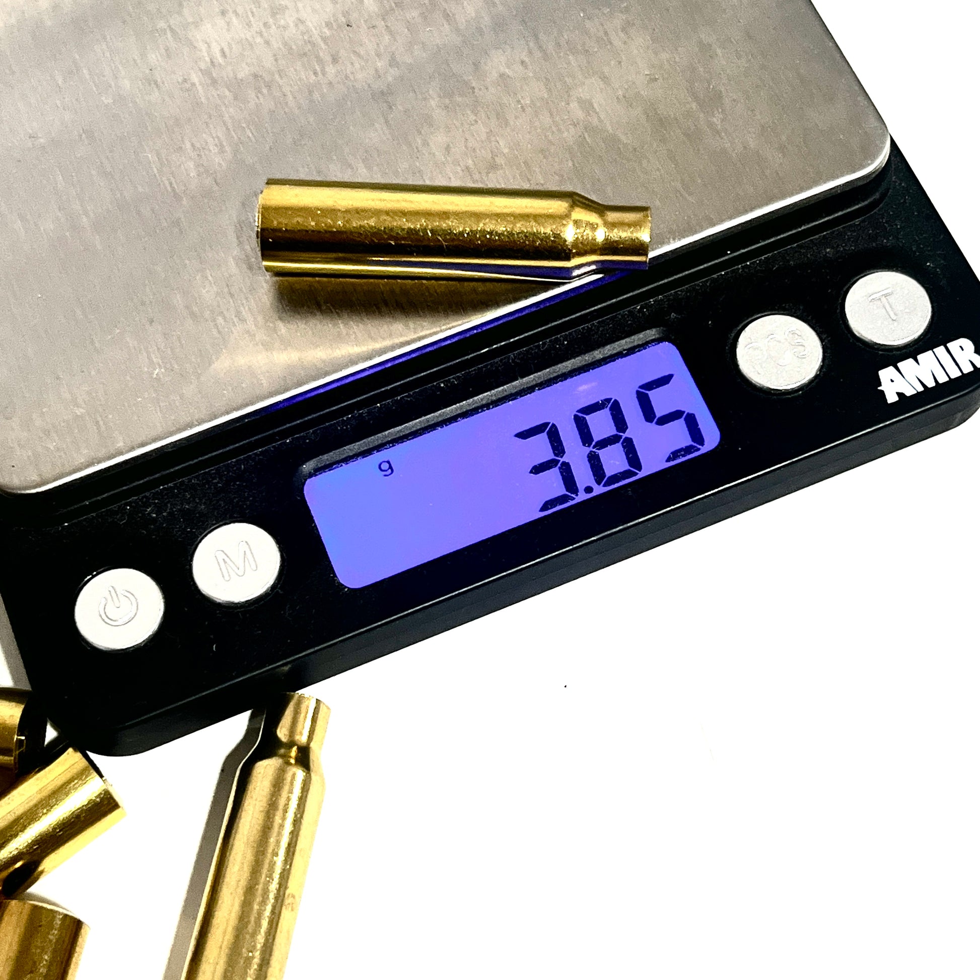 A single .223 brass bullet casing bead on a digital scale showing 3.85 grams, with loose casings in the background on a white background