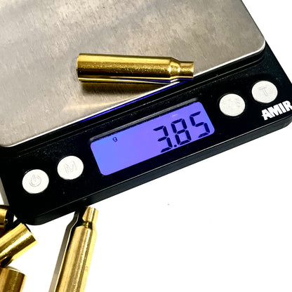 A single .223 brass bullet casing bead on a digital scale showing 3.85 grams, with loose casings in the background on a white background