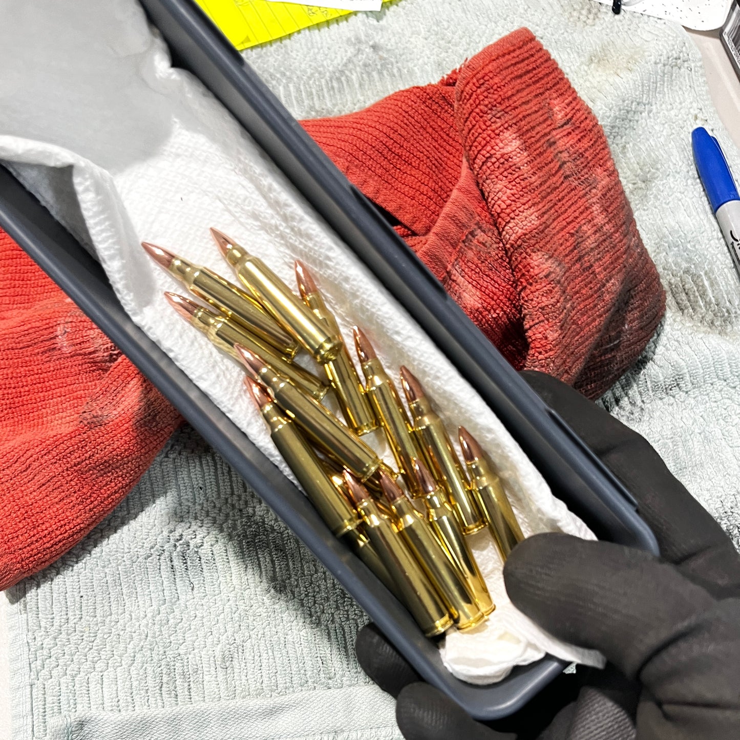 A container full of polished dummy rounds on the workbench with dirty rags