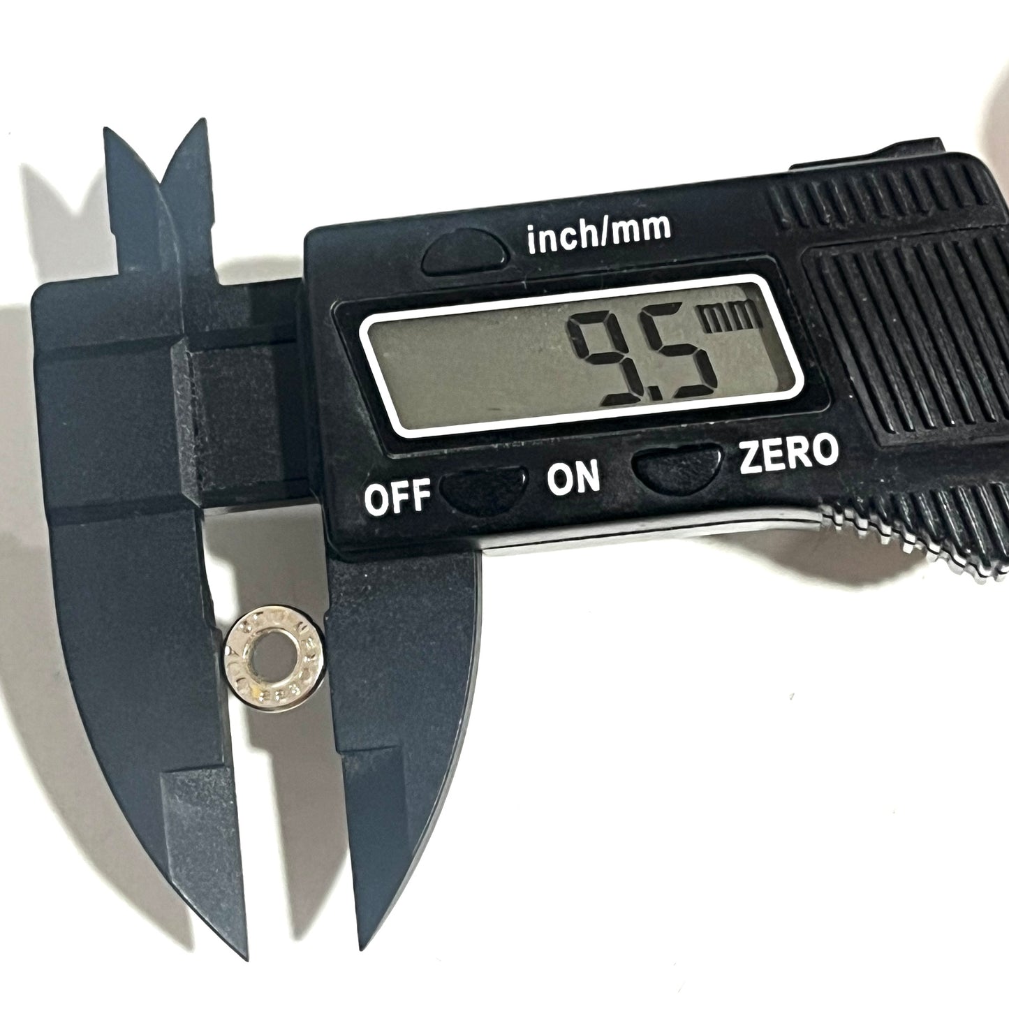 A used nickel cartridge slice beside a digital caliper displaying a 9.5 mm diameter reading.